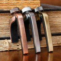 Three metal bookends with screw-top handles in copper, silver, and gold finishes, arranged side by side on a wooden surface in front of stacked books.