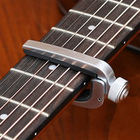 A close-up of a silver metal guitar capo clamped onto the fretboard of a dark brown guitar, with the adjustment knob visible on the right side.
