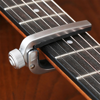A close-up of a silver metal guitar capo clipped onto a dark fretboard of an acoustic guitar, with the wood body and strings visible in the background.