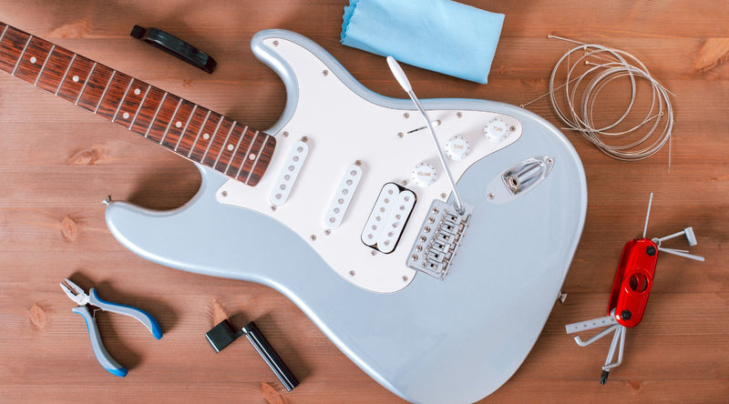 Light blue ST electric guitar laid with guitar maintenance tools on wooden table.
