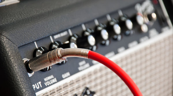 A red guitar cable plugs into a guitar amps control panel with multiple tone knobs.