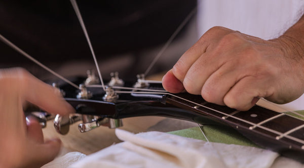 This close-up shot shows hands adjusting the truss rod at the guitar headstock, with one hand turning the tuning peg area and the other steadying the neck.