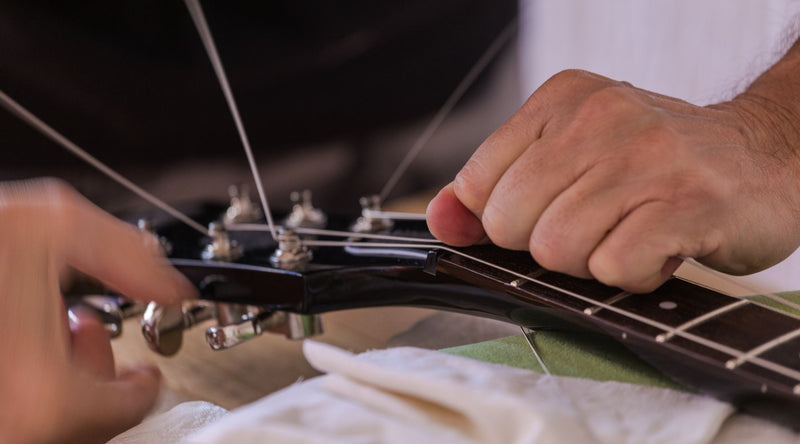This close-up shot shows hands adjusting the truss rod at the guitar headstock, with one hand turning the tuning peg area and the other steadying the neck.