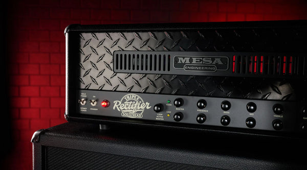 Mesa Rectifier tube amp head atop speaker cabinet, red brick wall backdrop.