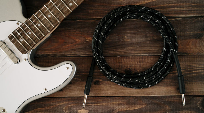Black woven guitar instrument cable coiled on rustic wooden planks next to white electric guitar, top view