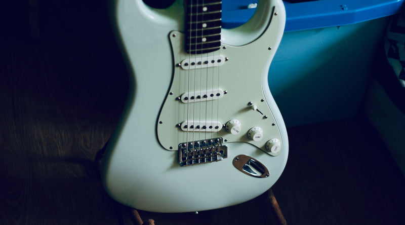 White electric guitar with blue pickguard on a dark background