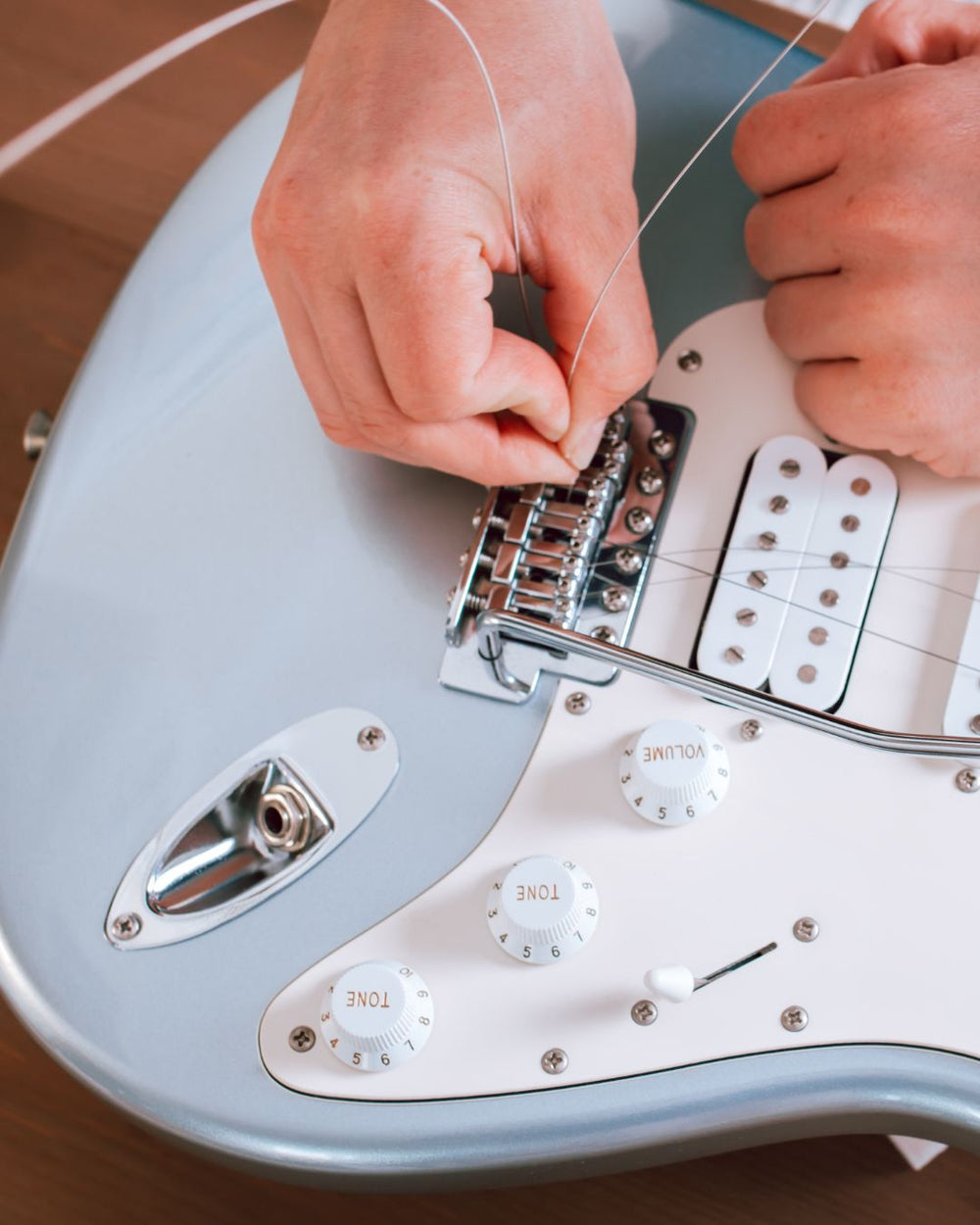 Person adjusting a guitar's bridge on a light blue electric guitar.