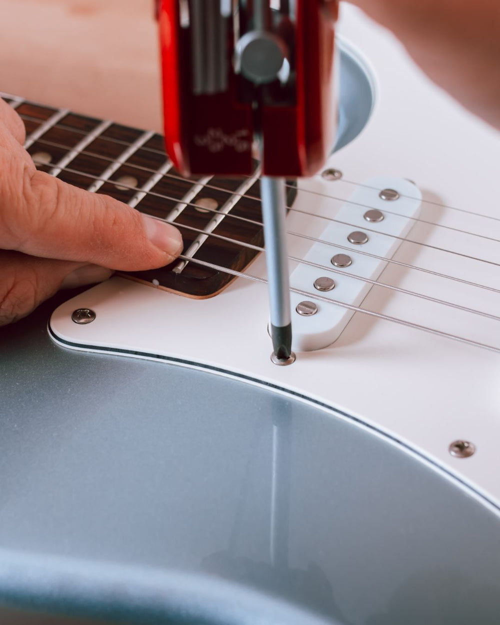 Person adjusting a guitar's bridge with a screwdriver