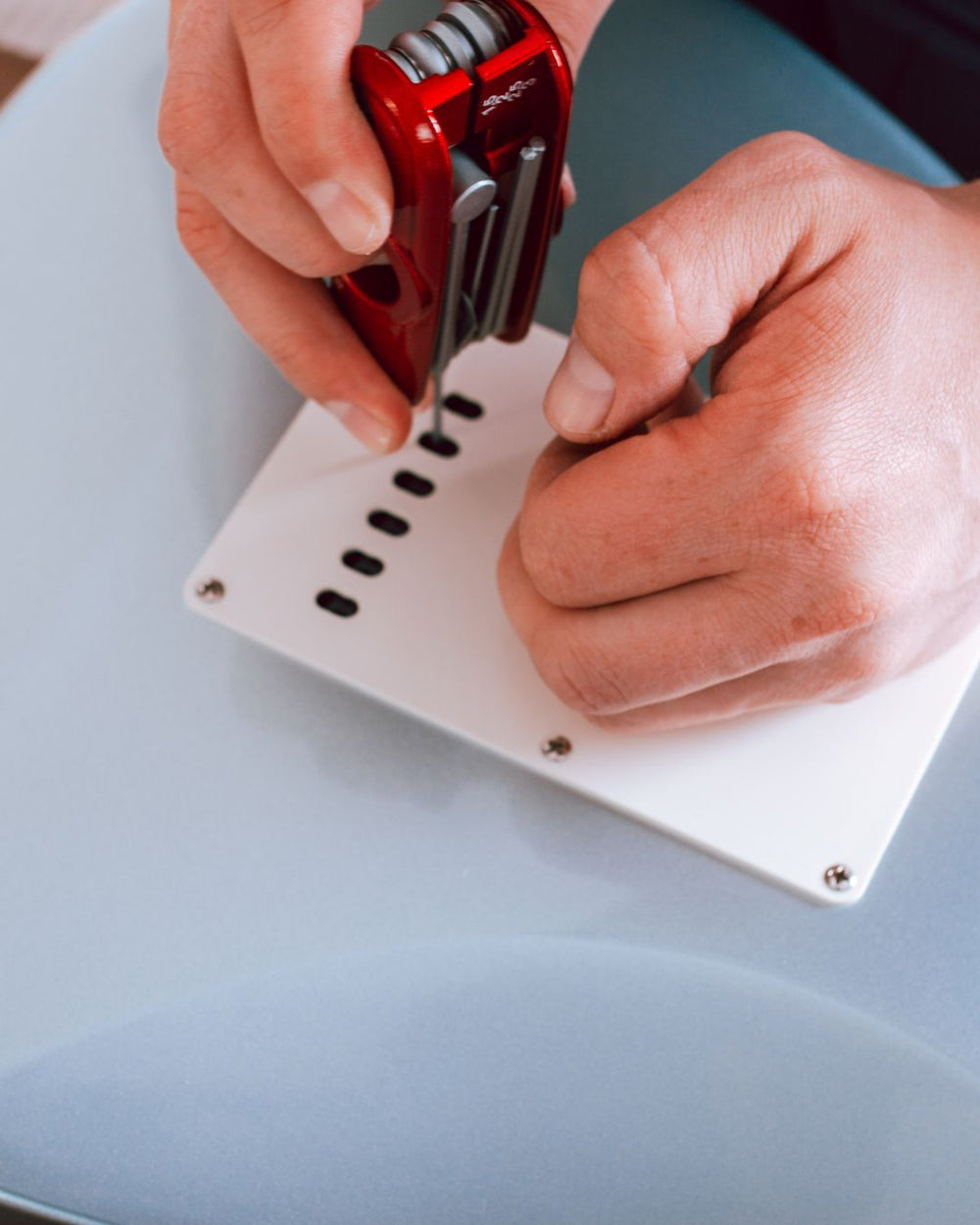 Person using a red hand exerciser on a white plate with holes.