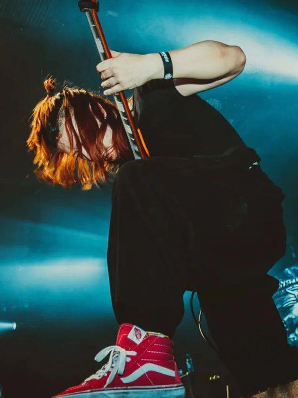 A person in a black outfit and red high-top sneakers poses with a microphone on stage under blue stage lighting.